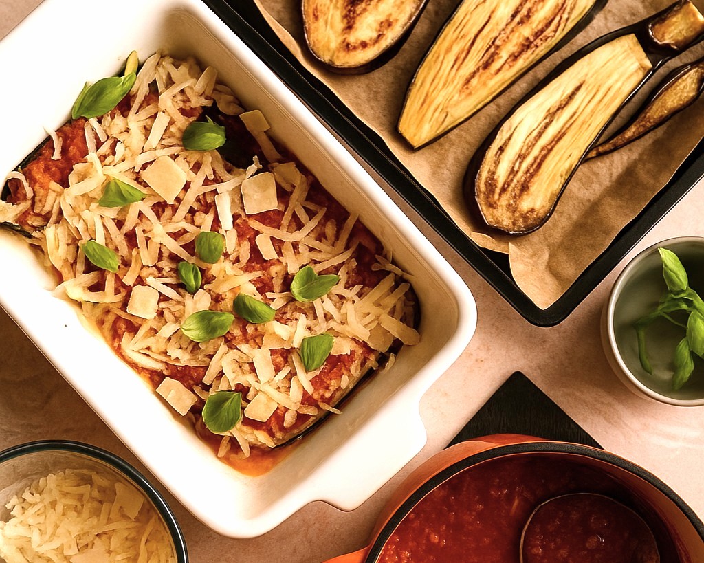 placing the baked aubergine in a white ceramic dish covered with grated cheese and parmigiana