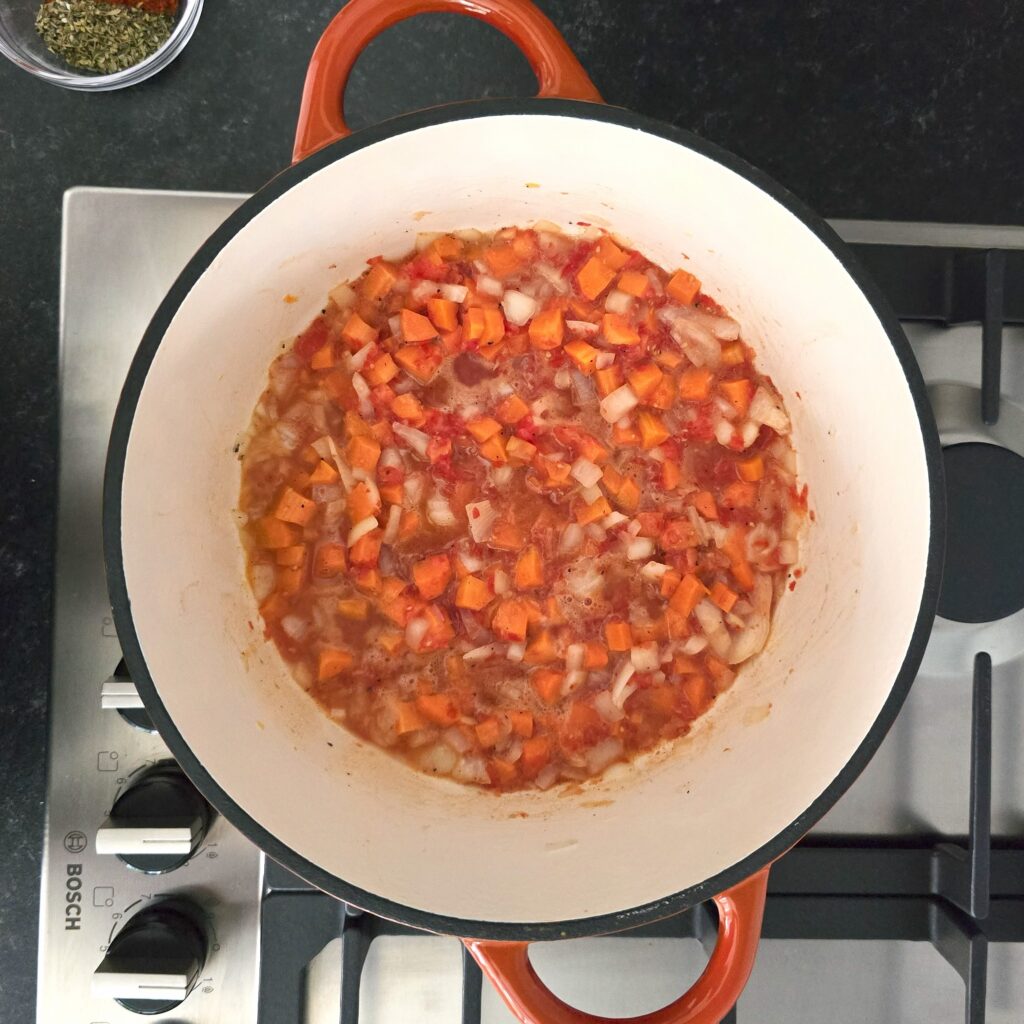 a pot with diced onion, carrots and tomato sauce, sauteed in oil