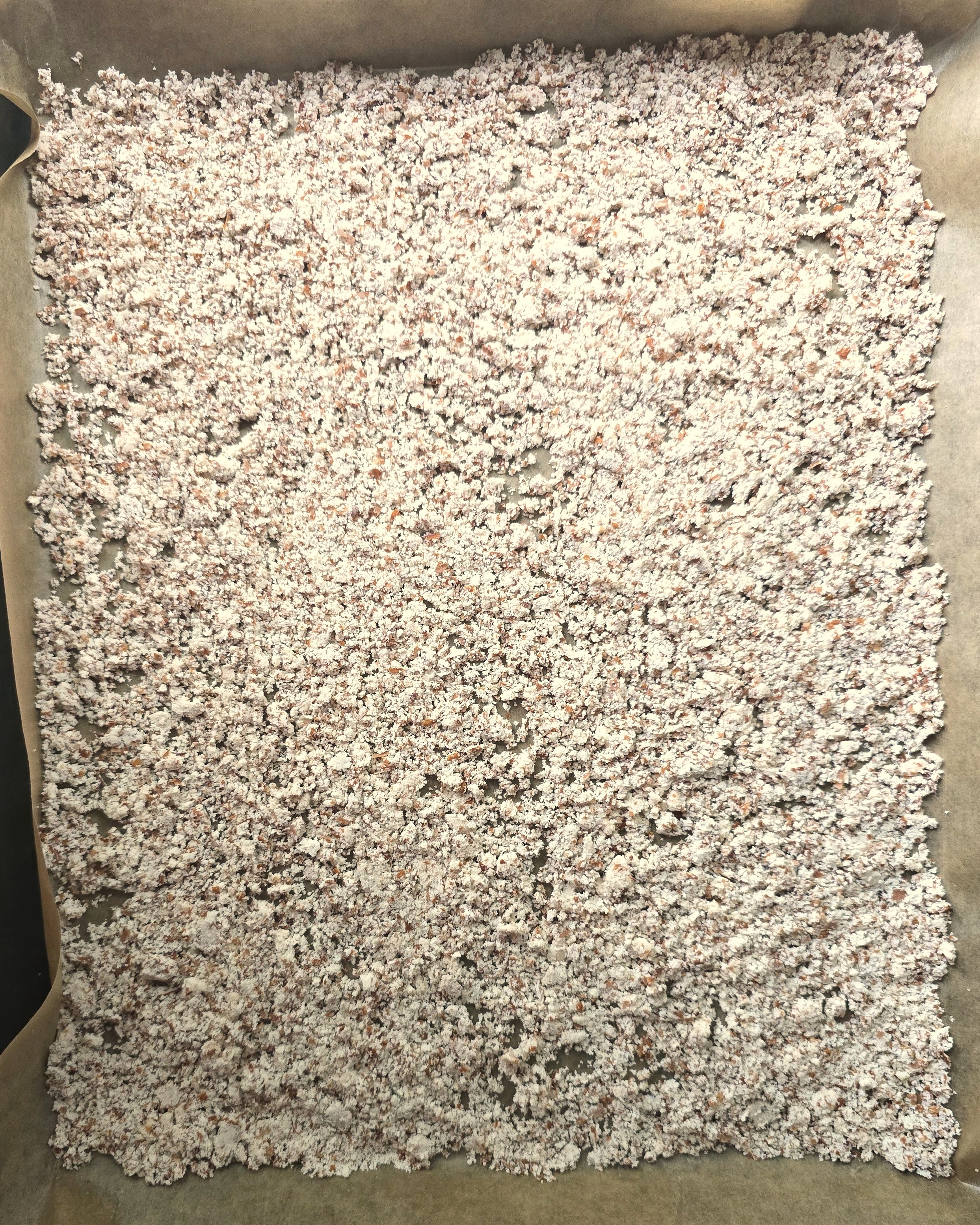 a baking tray with parchment paper with spread wet almond pulp ready to be dried in the oven