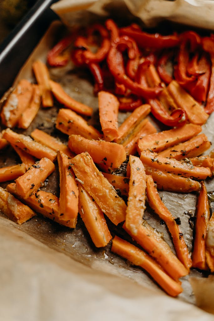 Deliciously roasted carrots and bell peppers seasoned with herbs on a baking tray.